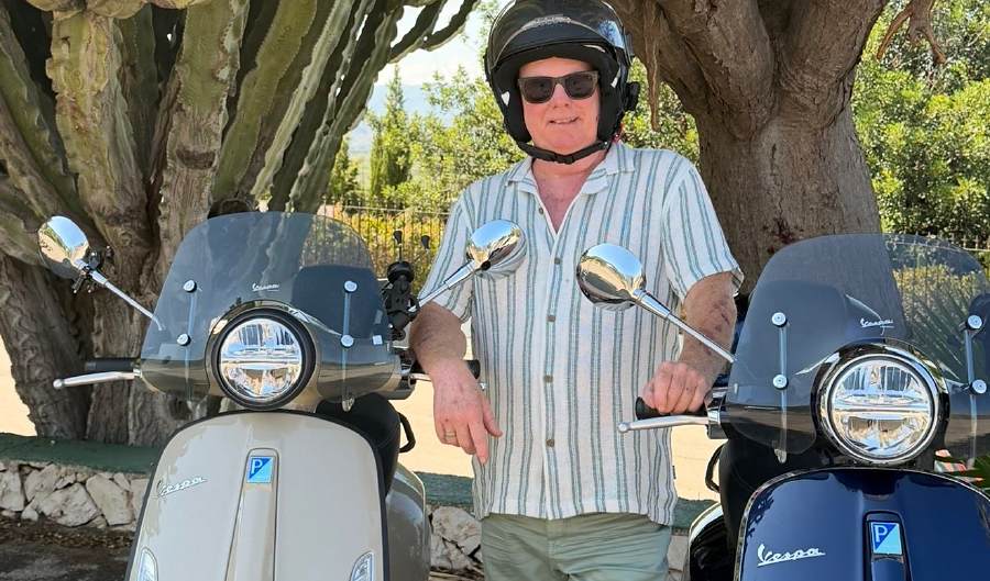A guide in a helmet standing between two Vespas, ready to leave